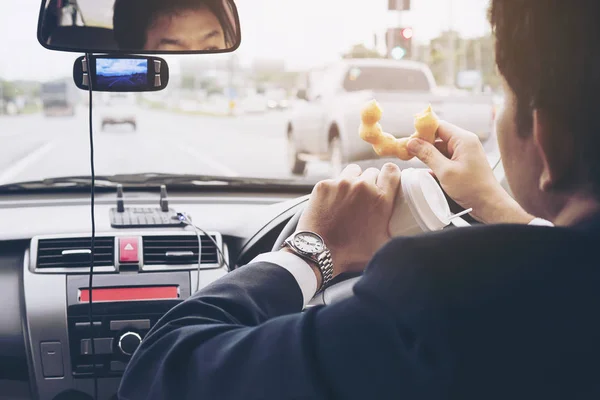 Man eating donuts with coffee while driving car - multitasking unsafe driving concept