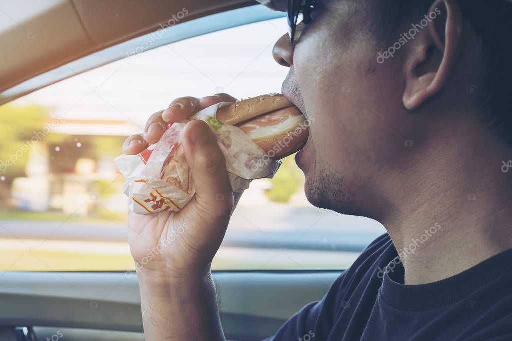 Man is dangerously eating hot dog and cold drink while driving a car