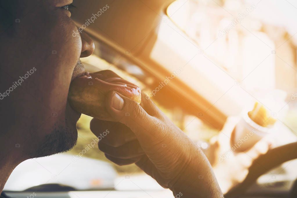Man eating donuts and potato chip while driving car - multitasking unsafe driving concept