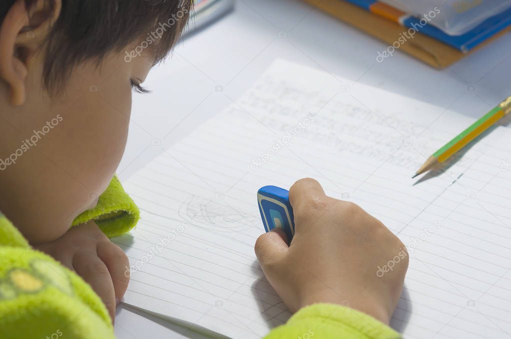 A boy is doing his homework, using an eraser