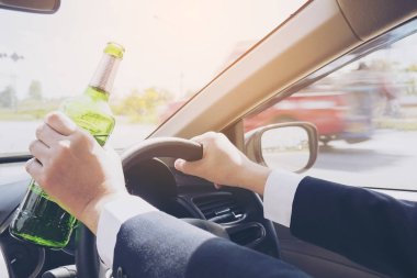 Bir araba sürüş sırasında bira şişesi tutan adam