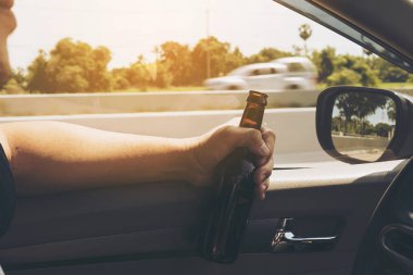 Bir araba sürüş sırasında bira şişesi tutan adam