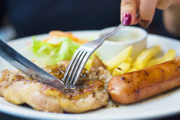 Closeup of woman eating chicken steak with sausage, french fries and salad dish