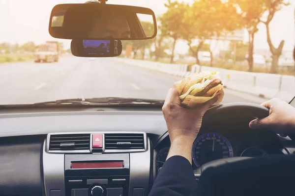 Man driving car while eating hamburger