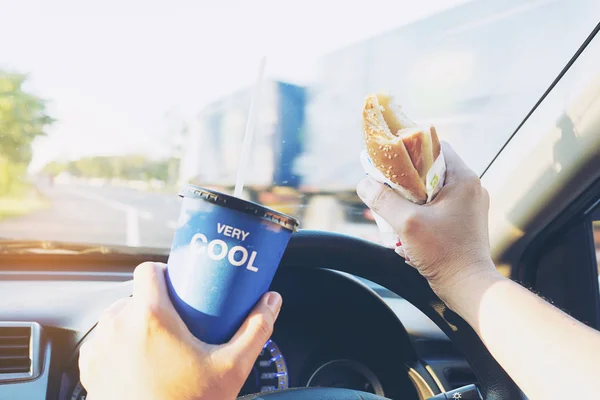 Man is dangerously eating hot dog and cold drink while driving a car