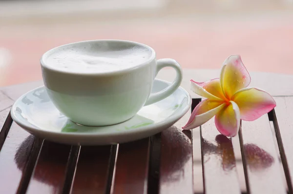 Plumeria flower with coffee cup on wooden table focusing at upper petal of plumeria.