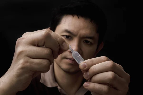 Man preparing eye drop medicine healing his eye pain with black background - health care eye medicine with people concept