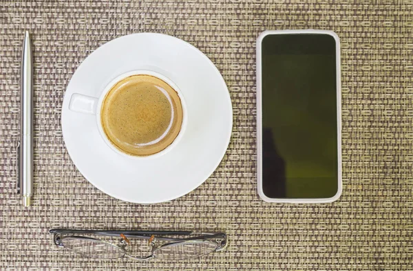 Top view of coffee with pen glasses and mobile phone over weave bamboo background
