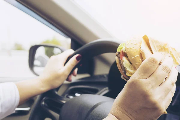 Lady driving car while eating hamburger
