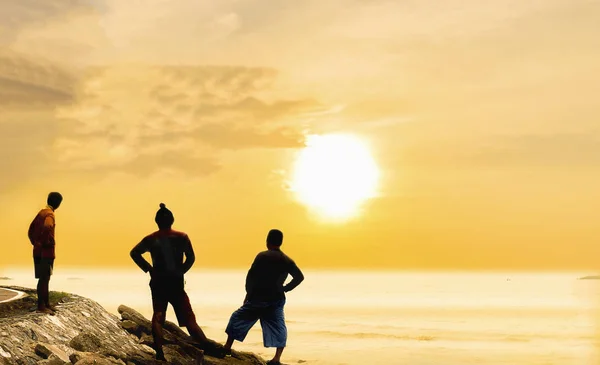 Warm tone silhouette photo of fisherman are standing on beach looking to the sea