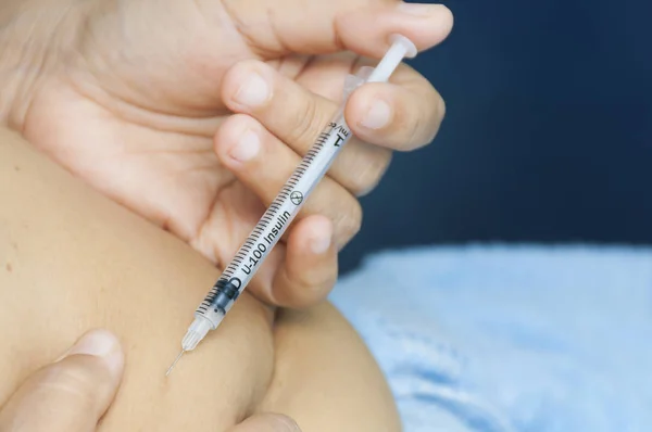 A lady is injecting insulin into her stomach. Photo is focus at syringe.