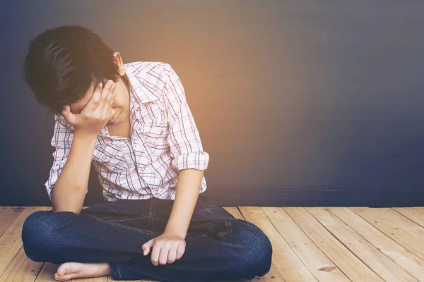 Sad Asian boy sitting on wood floor