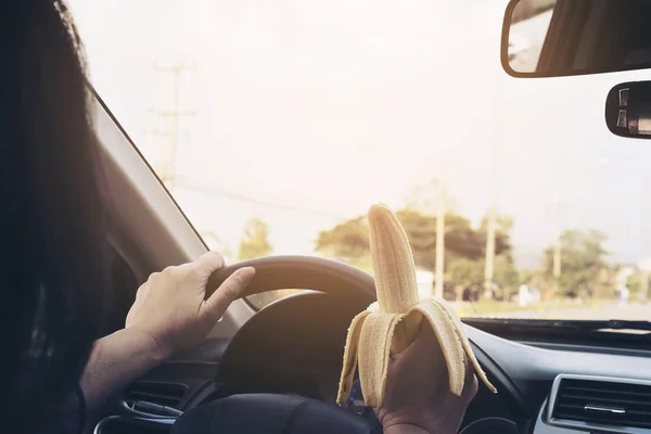 Lady eating banana while driving car dangerously