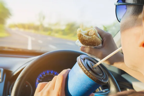 Man is dangerously eating hot dog and cold drink while driving a car