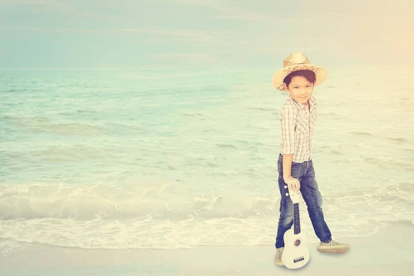 ビーチの背景にウクレレで立っているアジアの 歳の少年 — ストック写真