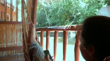 Bayan relax bambu sal üzerinde hamakta mutlu siting ve cep telefonuyla Tayland