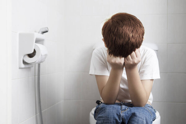 Asian boy sitting on toilet bowl holding tissue paper  - health problem concept