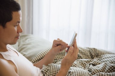 Sabah - her gün hayat kavramı teknolojisinde yatağa uyku modundan çıkarma sırasında cep telefonu kullanarak adam