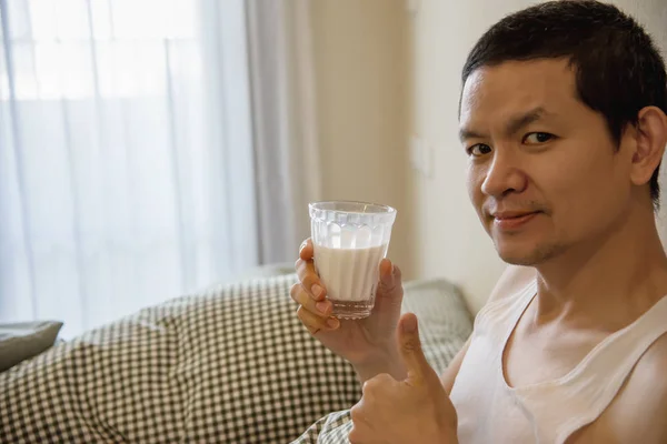 Asian man drink milk after wake up in the morning sitting on a bed - health care concept