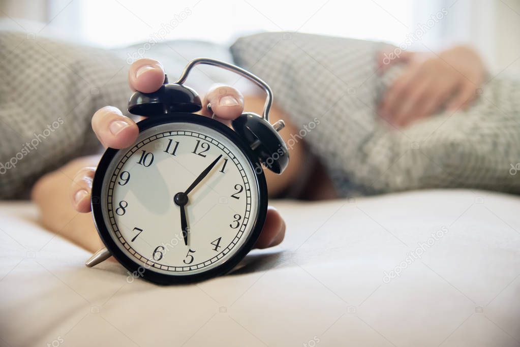 Sleepy man holding the alarm clock in the morning with late wake up - every day life at home concept