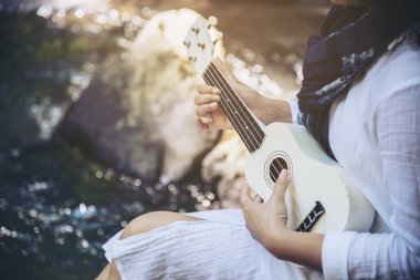 Kadınlar şelalenin yanında ukulele çalar - insanlar ve müzik aleti doğa konseptinde yaşam tarzı 