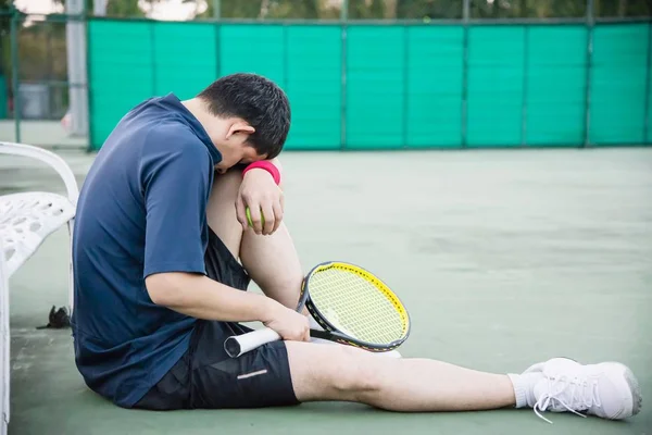 Sad tennis player sitting in the court after lose a match - people in sport tennis game concept