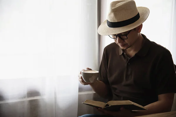 Relax Asian man drink coffee and read book in a modern style coffee shop - people with coffee cup easy lifestyle concept