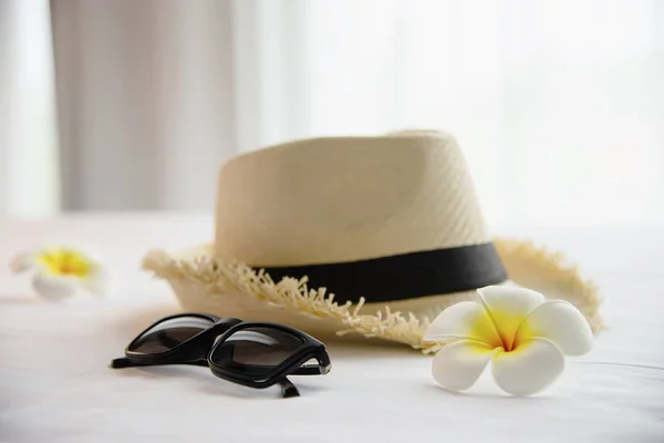 Tourist stuff hat sun glasses and plumeria flower in white bed room - happy relax vacation holiday and hotel concept