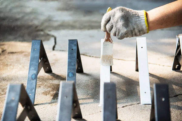 Man is coating white color for steel furniture part - painter at work concept