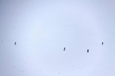 Beyaz karlı düz üzerinde dört uzak kayakçı