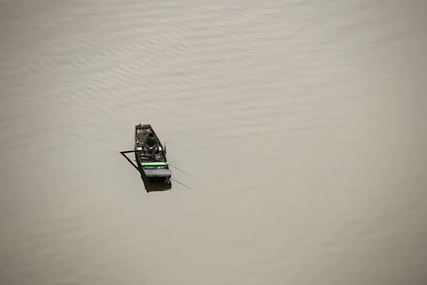 Barco de pesca con el hombre sentado en él en la superficie de agua marrón calma — Foto de Stock