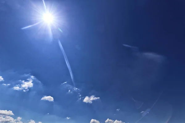 Sol y pocas pequeñas nubes en el cielo azul con la llamarada de la lente — Foto de Stock