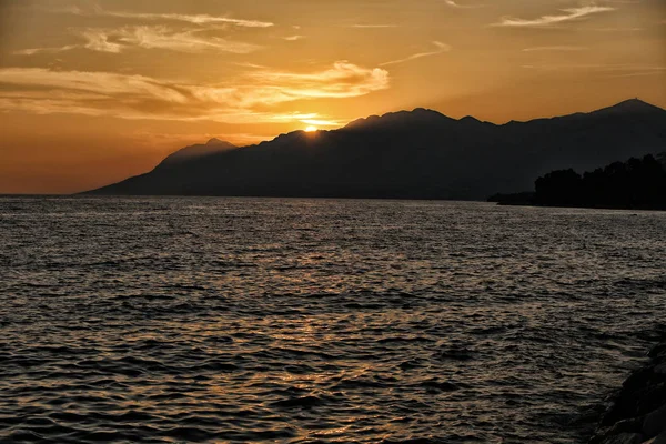 Puesta de sol sobre las montañas junto al mar ondulado — Foto de Stock