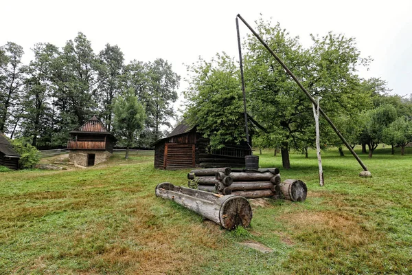Vecchio pozzo in legno su giardino alberato con cottage in legno — Foto Stock
