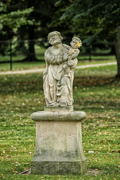 公園の台座の上に金色の花を持つ老人ホリング子の像 — ストック写真