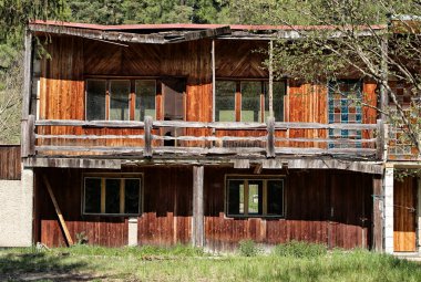 Balkonlu eski ahşap bir ev, çatısı sökülmüş ve kahverengi duvarları var.