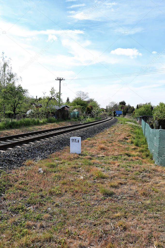 Straight railway under electricity lines with white milestone in grass