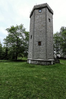 Ağaçların ve çimenlerin arasında altıgen taş görünümlü kule