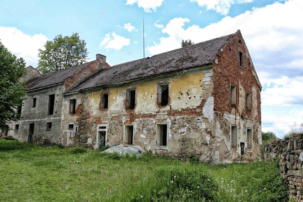 Large abandoned brick house with glassless windows and cracked facade