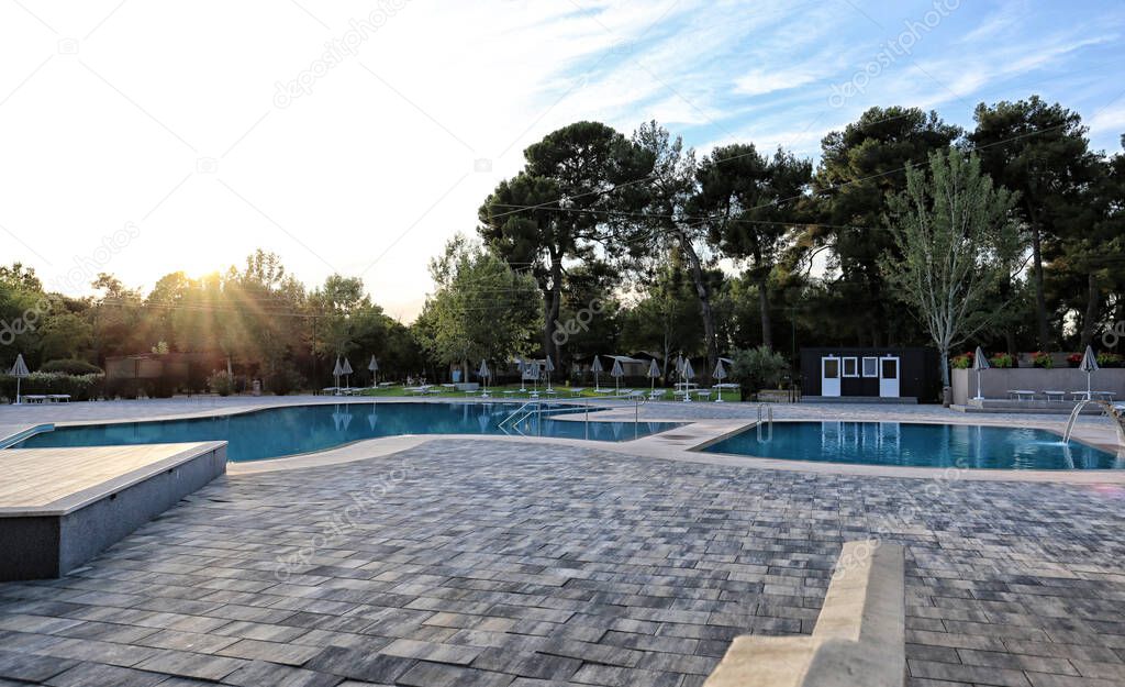 Empty pools with tiled floor and small podium by the trees on evening