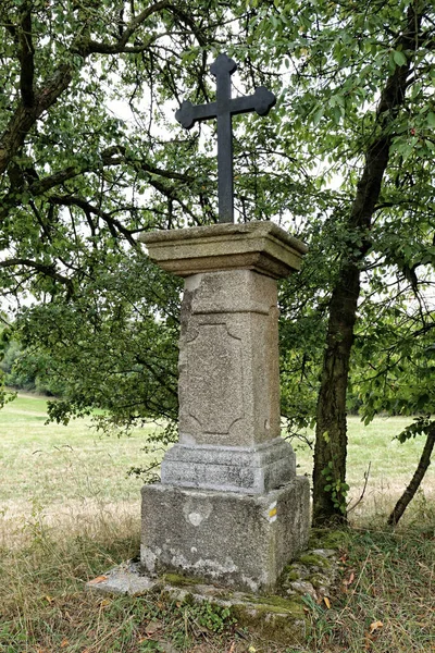 フィールド上の木による花崗岩の石の台座上の古い歴史的な黒い金属の十字架 — ストック写真