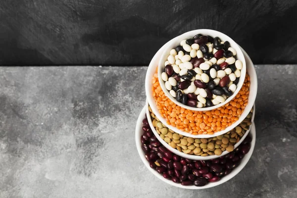 Assortment of beans (red lentil, green lentil, chickpea, peas, red beans, white beans, mix beans, mung bean) on gray background. Copy space. Food background