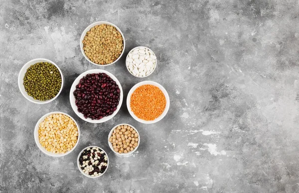 Assortment of beans (red lentil, green lentil, chickpea, peas, red beans, white beans, mix beans, mung bean) on gray background. Top view, copy space. Food background
