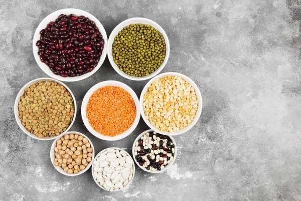 Assortment of beans (red lentil, green lentil, chickpea, peas, red beans, white beans, mix beans, mung bean) on gray background. Top view, copy space. Food background