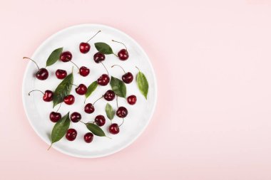 Olgun kiraz ve yeşil yaprakları pembe bir arka plan üzerinde. Görünümü en çok, uzay kopyalayın. Gıda arka plan