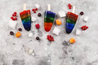 Gökkuşağı renkli dondurma ahududu sarı ve kırmızı, böğürtlen, frenk üzümü ile buzlu şeker ahşap ile gri arka plan üzerinde sopa. Görünümü en çok, uzay kopyalayın. Gıda arka plan