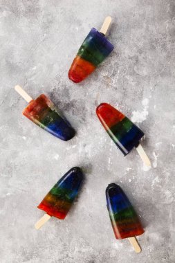 Gökkuşağı renkli buz gri arka plan üzerinde ahşap sopa ile birkaç buzlu şeker krem. Üstten görünüm. Gıda arka plan