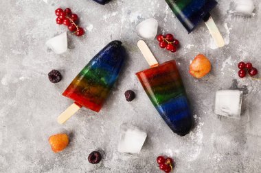 Gökkuşağı renkli dondurma ahududu sarı ve kırmızı, böğürtlen, frenk üzümü ile buzlu şeker ahşap ile gri arka plan üzerinde sopa. Üstten görünüm. Gıda arka plan