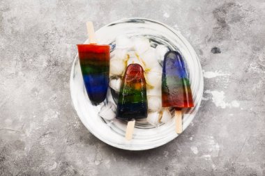 Gökkuşağı renkli dondurma dondurma ahşap ile mermer plaka gri arka plan üzerinde sopa. Üstten görünüm. Gıda arka plan