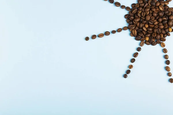 Sun made of coffee beans on blue background. Concept begins morning with coffee. Top view, copy space. Food background